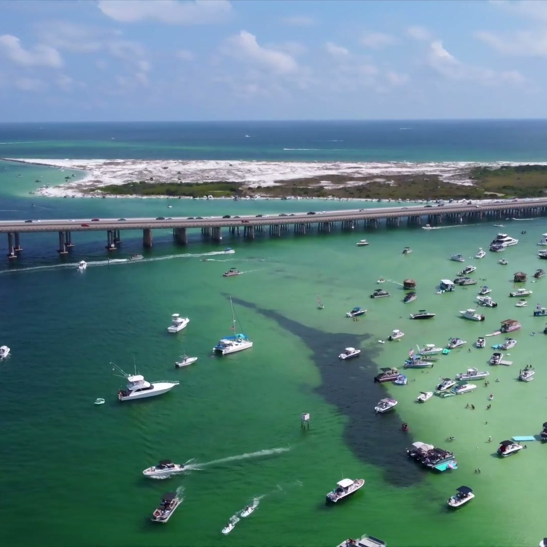 Aerial view of Crab Island in Destin, FL, with the Destin bridge and boats anchored on the sandbar